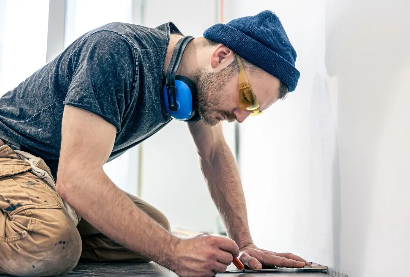 A male worker is laying laminate flooring on the floor.